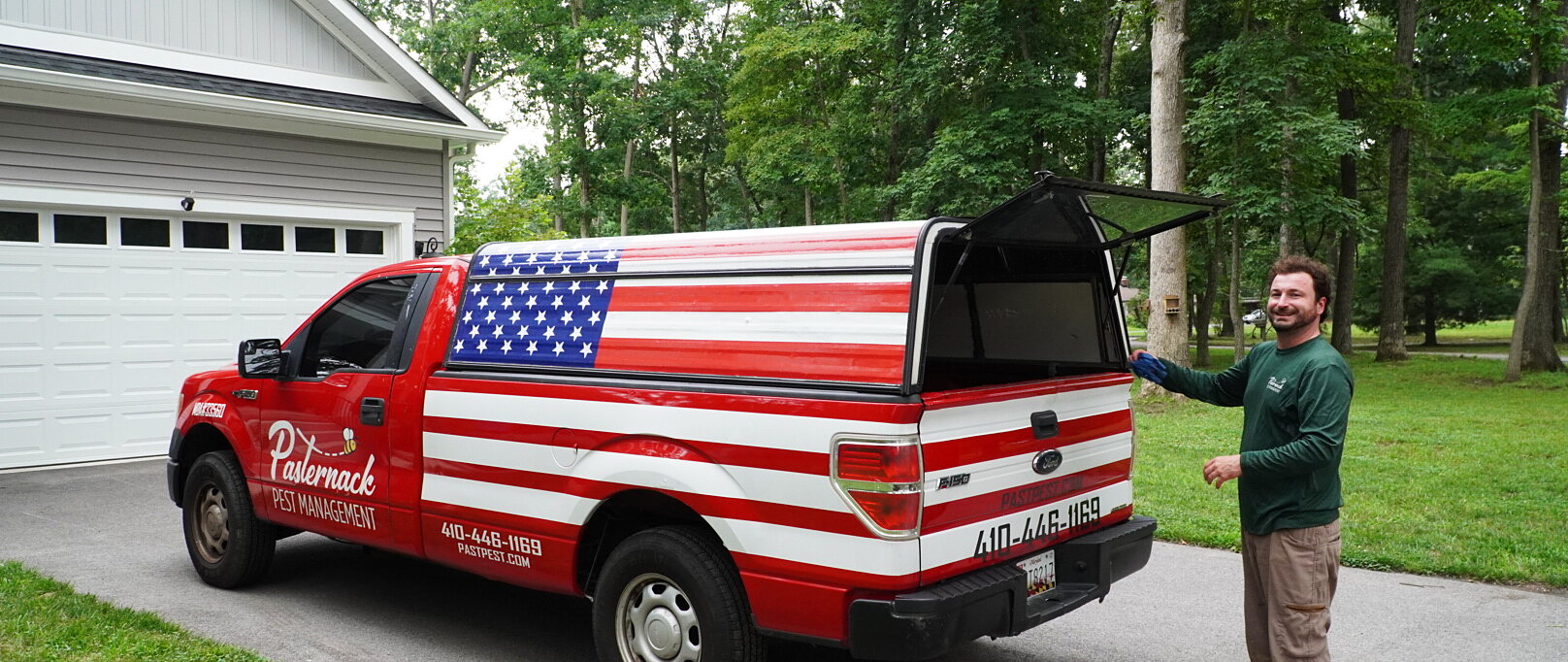 Erik Pasternack with Pasternack Pest Management's flag-wrapped service truck in a customer's driveway